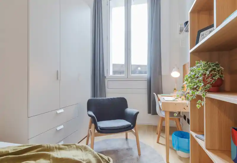 Rincón de dormitorio luminoso y acogedor con un sillón cómodo, armario empotrado y escritorio junto a la ventana: ideal para relajarse o trabajar.