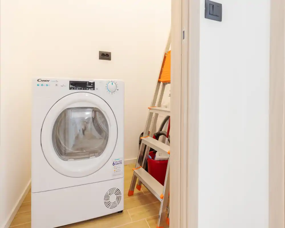 Petite buanderie/utility avec sèche‑linge frontal et matériel de nettoyage—sol lumineux et propre, espace pratique pour un appartement.