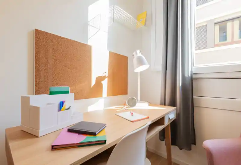 Angolo studio luminoso e ordinato con scrivania in legno, pannelli di sughero e lampada da tavolo vicino alla finestra — perfetto per lavoro o studio.