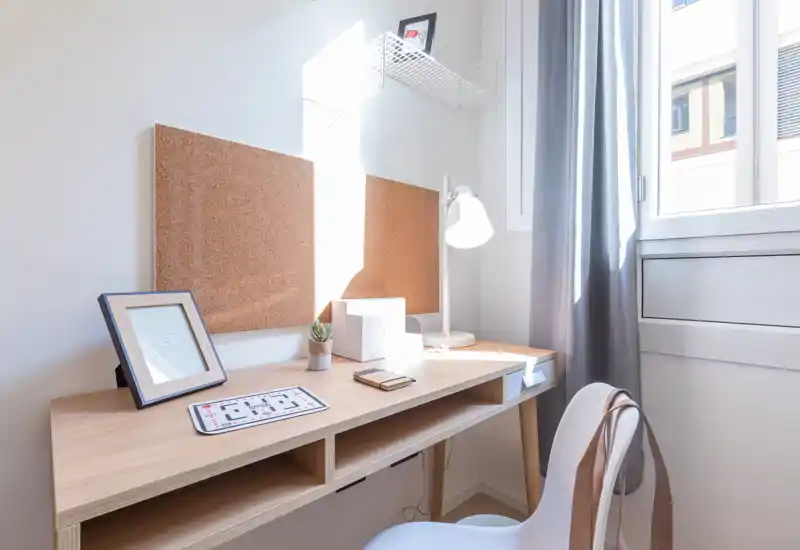 Bright, minimal home office corner with a wooden desk, cork pinboards, task lamp and a comfortable chair by a large window — ideal for focused work.