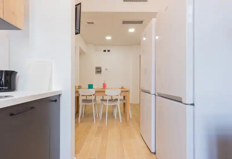 Simple, modern dining area with a wooden table and four white chairs set on warm wood-effect flooring. Bright, minimal styling suitable for short-term rentals or apartment listings.