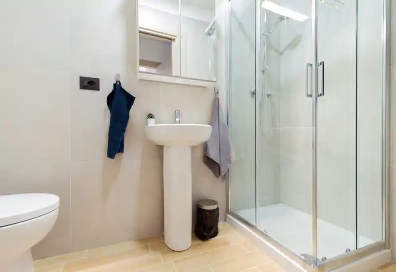 Bright, modern bathroom with a glass-enclosed shower, pedestal sink, and contemporary tiles — clean and well-lit space ideal for guest listings.
