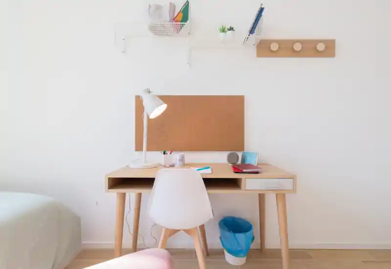 Angolo camera luminoso e minimal con scrivania in legno e una piccola porzione del letto visibile a sinistra; ideale per studiare o lavorare da remoto.