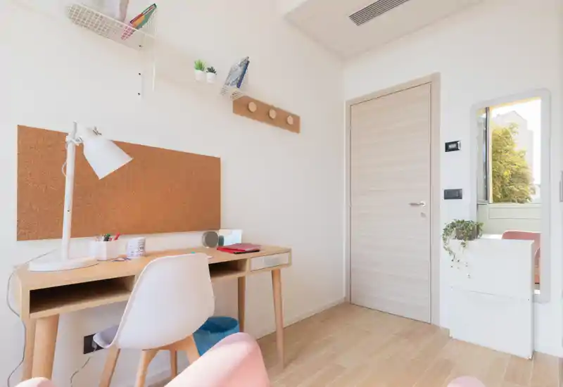 Angolo luminoso e minimale della camera con scrivania in legno, bacheca in sughero e una sedia confortevole — perfetto come area studio nella stanza da letto.