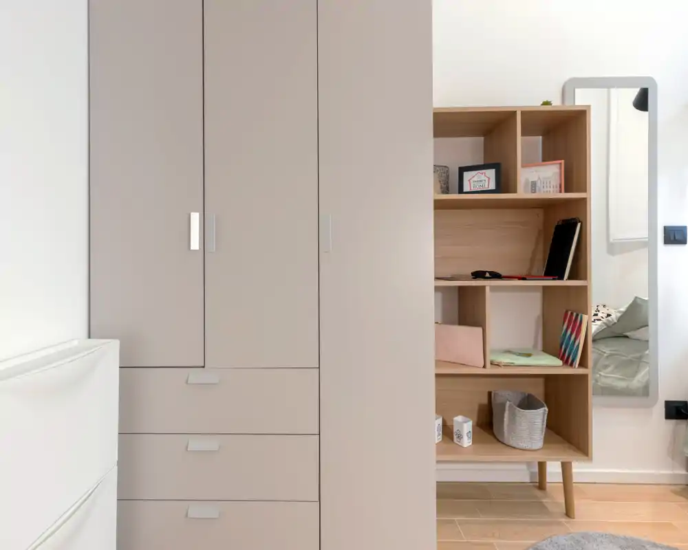 Coin de chambre soigné avec une grande armoire et des étagères ouvertes ; une petite partie du lit est visible à droite. Finitions modernes et lumière abondante pour un espace calme et fonctionnel.
