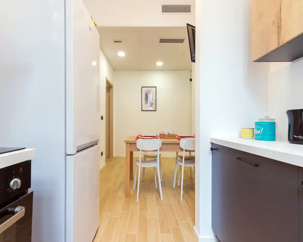 Espace repas lumineux et moderne adjacent à la cuisine, avec une table en bois pour quatre et une décoration minimaliste.