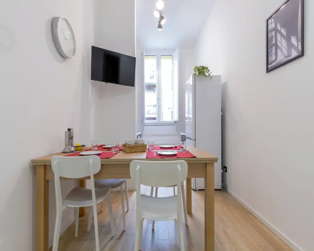 Coin repas lumineux et minimaliste avec une table en bois pour quatre personnes, chaises blanches et lumière naturelle par la fenêtre ; compact et bien agencé pour un petit appartement.
