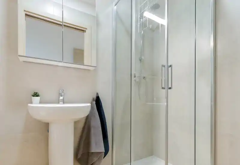 Bright, modern bathroom with a pedestal sink, mirrored cabinet and a glass-enclosed shower; neutral tiles and tidy styling.
