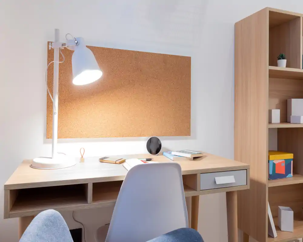 Rincón de trabajo luminoso y ordenado con escritorio de madera, lámpara blanca y panel de corcho — ideal para estudiar o trabajar.