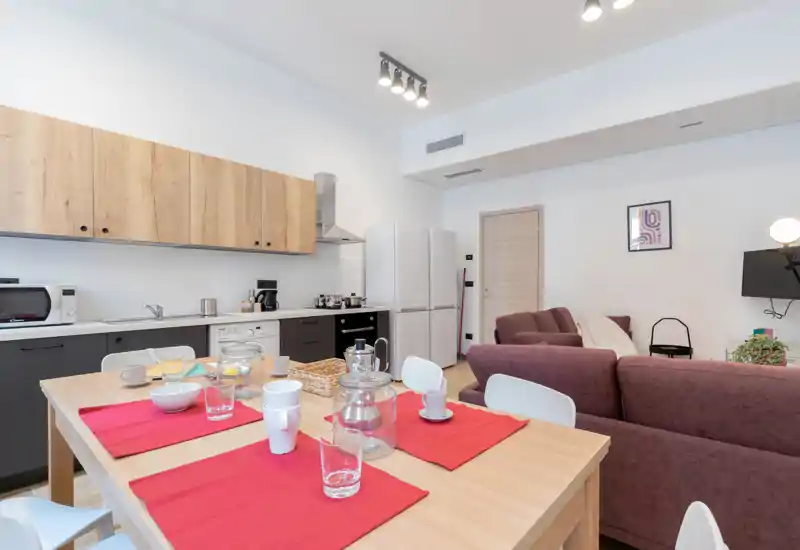 Open-plan living area with a kitchen and dining table in the foreground, comfortable sofa seating and bright, modern finishes — ideal for a small apartment stay.