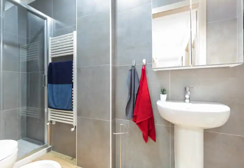 Modern compact bathroom with walk-in shower, pedestal sink, heated towel rail and neutral grey tiles. Bright, clean and well-styled — ideal for rental listings highlighting a contemporary bathroom.