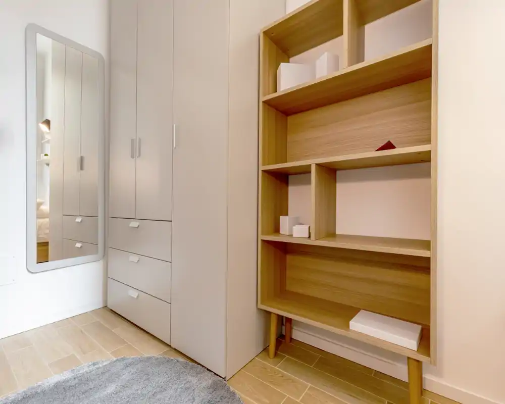 Rincón de dormitorio ordenado con armarios empotrados, espejo de cuerpo entero y estanterías de madera; acabados modernos y suelo de madera clara que dan una apariencia limpia y minimalista.