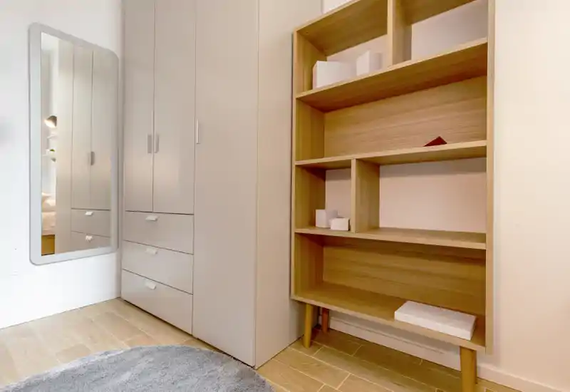 Angolo di camera ordinato con armadi a incasso, specchio a figura intera e scaffalatura in legno; finiture moderne e pavimento in legno chiaro per un aspetto pulito e minimale.