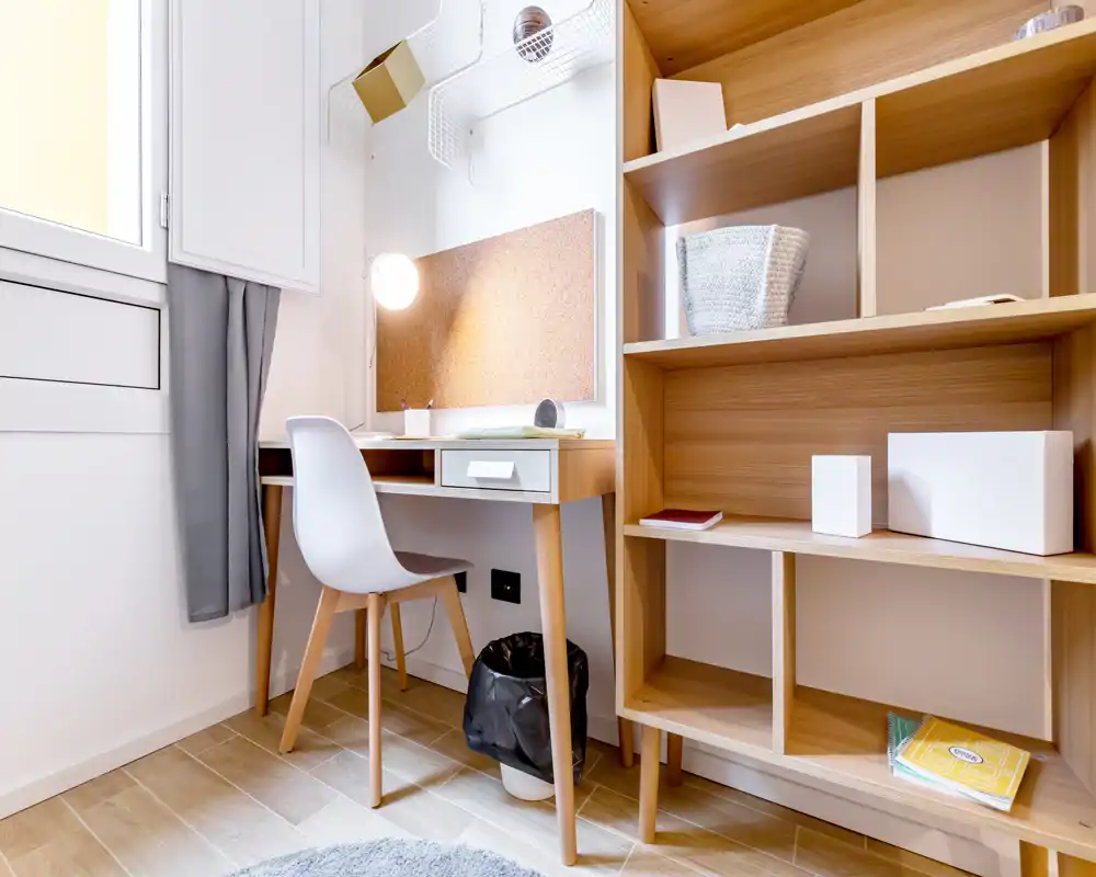 Pequeño rincón de estudio luminoso con escritorio de madera, silla y estanterías abiertas; ideal para trabajar desde casa.