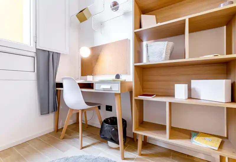 Small, bright study corner with a wooden desk, chair and open shelving; ideal for a work-from-home setup.
