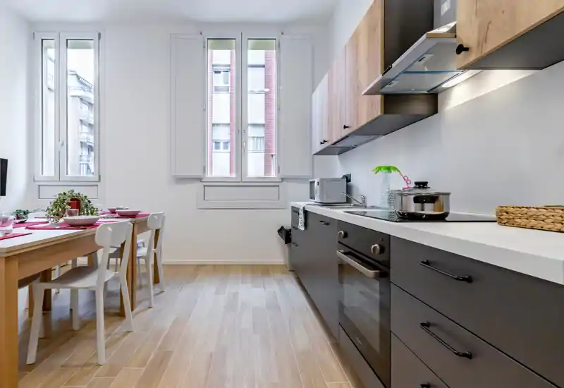 Bright modern kitchen with dark lower cabinets, wood-effect upper cabinets and a wooden dining table set near the window; compact, clean and ready for meals.