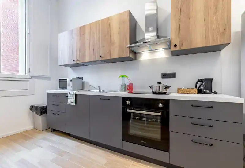 Modern fitted kitchen with matte gray lower cabinets, wooden upper cupboards, built-in oven, extractor hood and a clean white countertop — bright and well organized.