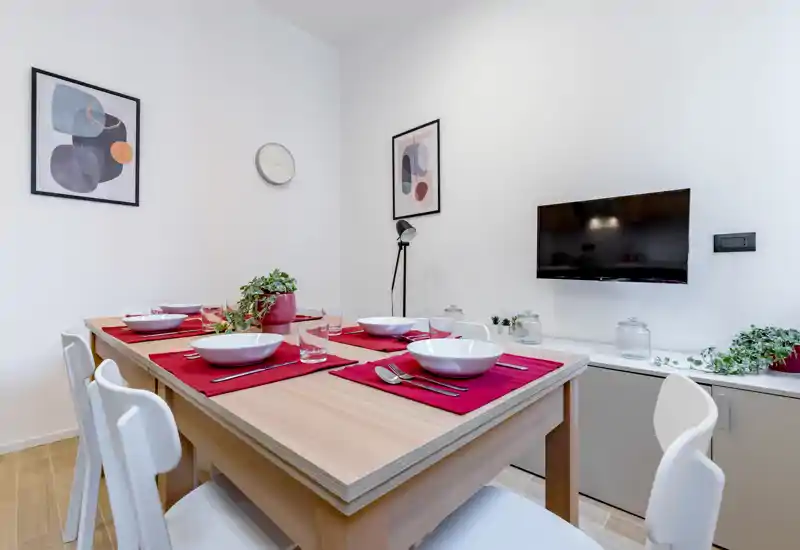 Bright, modern dining area with a wooden table set for four, red placemats, white chairs and decorative plants — ideal for cozy meals.