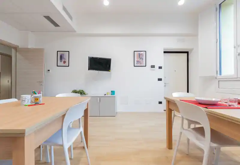 Bright, modern living area with light wood tables, white chairs and minimal decorative accents; well lit and ideal for shared meals or work.