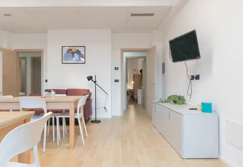 Bright, modern living area with a dining table, white chairs, a small sofa and wall-mounted TV — clean styling ideal for short-term rentals.