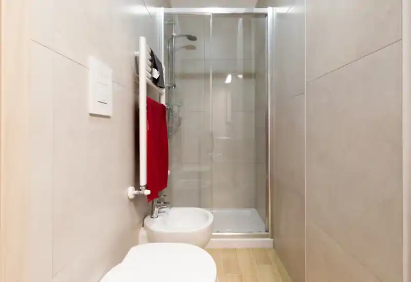 Compact modern bathroom with a glass shower enclosure, wall-mounted radiator with towels, bidet and toilet — bright, clean and efficiently arranged.