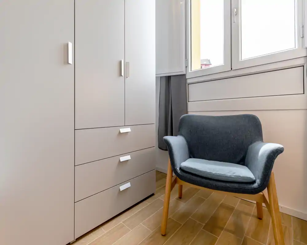 Angolo luminoso e minimale con una poltrona moderna accanto a un armadio a incasso e una finestra grande — perfetto come angolo lettura o piccolo soggiorno.