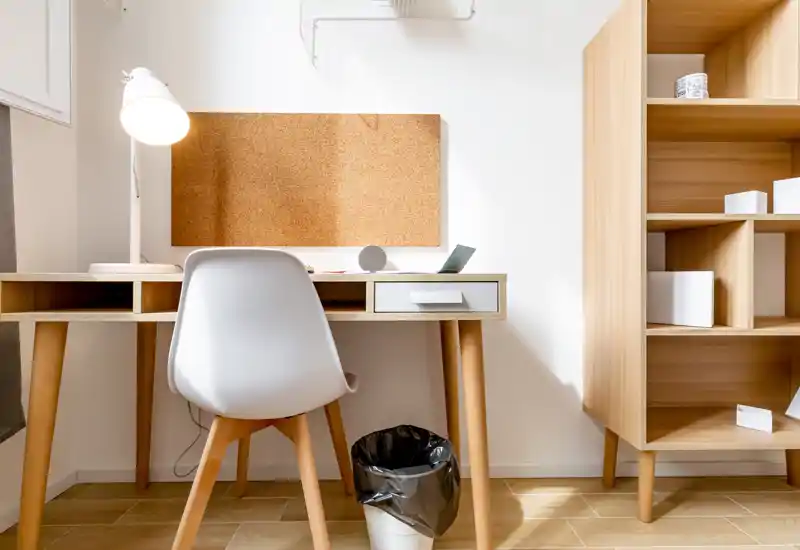 Angolo ufficio luminoso e minimale con scrivania in legno, sedia bianca, lampada da tavolo e pannello in sughero — uno spazio ordinato perfetto per lavoro o studio.