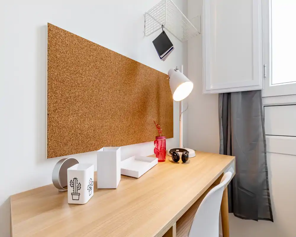 Rincón de estudio compacto y luminoso con escritorio de madera, corcho para notas, lámpara de escritorio y silla — ideal para trabajar o estudiar.