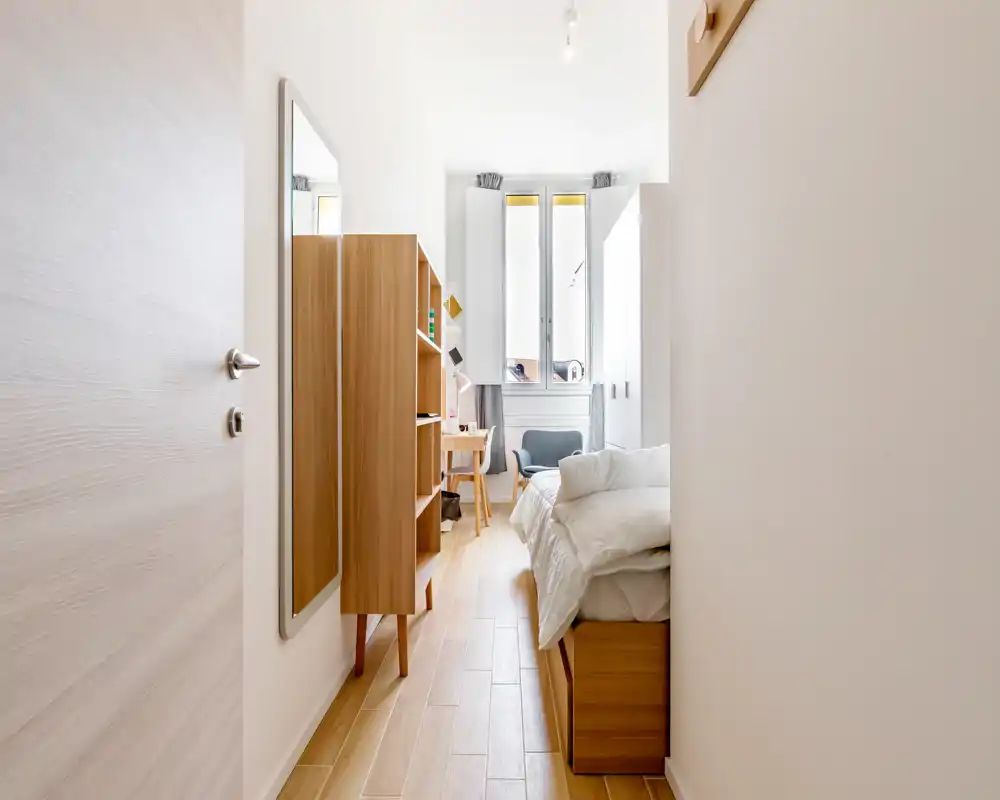 Dormitorio moderno y luminoso con estructura de cama de madera, ropa de cama blanca, escritorio junto a la ventana y muebles de madera que crean un ambiente acogedor.