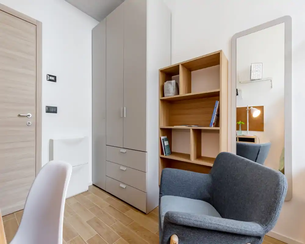 Coin salon lumineux et élégant avec un fauteuil confortable, une étagère et une grande glace — idéal pour se détendre ou lire.
