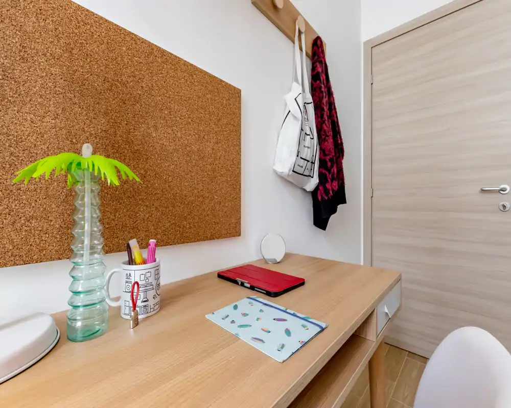 Petit espace d'entrée ou alcôve de couloir soigné avec bureau en bois, patères et porte fermée — lumineux et bien rangé pour les clés ou notes rapides.