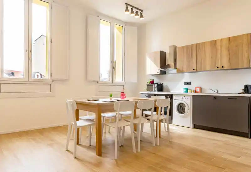 Bright modern kitchen with an integrated dining table for six. Light wood cabinets, large windows and clean design create an inviting space for cooking and casual meals.