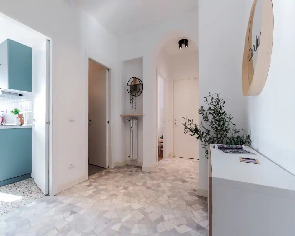 Ingresso luminoso e moderno con consolle decorativa, pianta e pavimento a mosaico; la cucina è visibile attraverso una porta aperta.