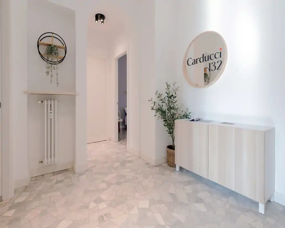 Ingresso luminoso e minimal con mobile console in legno chiaro, pianta in vaso e specchio decorativo. Il pavimento in stile terrazzo e le pareti bianche creano una prima impressione ariosa.