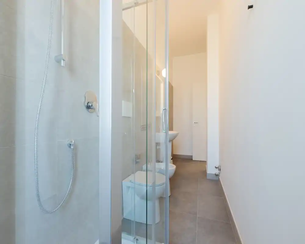 Bagno moderno e luminoso con doccia a vetro, sanitari sospesi e piastrelle in toni neutri; arredi lineari e design essenziale.