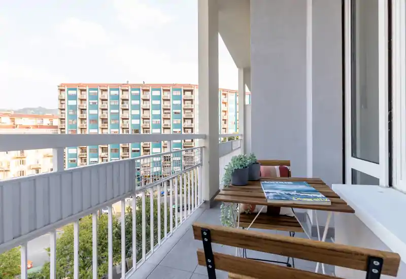 Sunny furnished balcony with a small wooden table and two folding chairs, potted plants and city views — ideal for morning coffee.