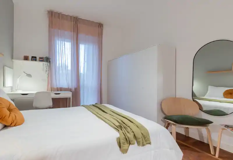 Chambre moderne et lumineuse avec lit bien fait, textiles doux et coussins chaleureux ; grand placard et bureau près de la fenêtre pour un espace fonctionnel et cosy.