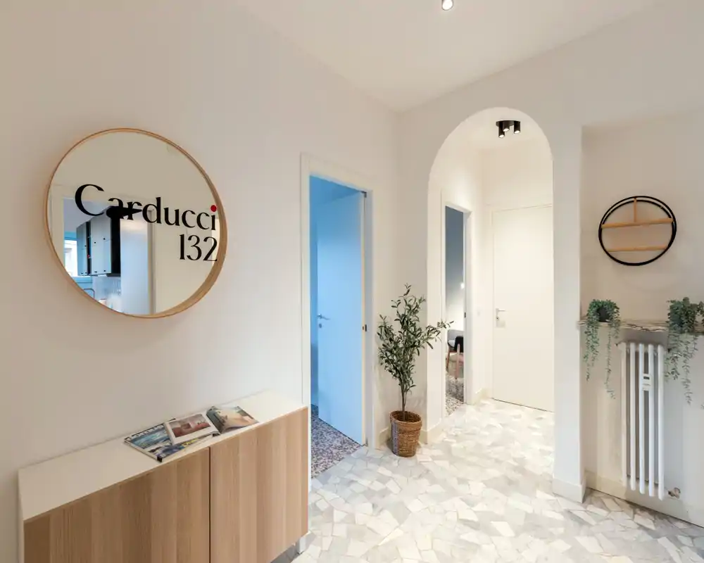 Ingresso luminoso e moderno con specchio rotondo decorativo, mobile console e pavimento piastrellato — un primo impatto accogliente.