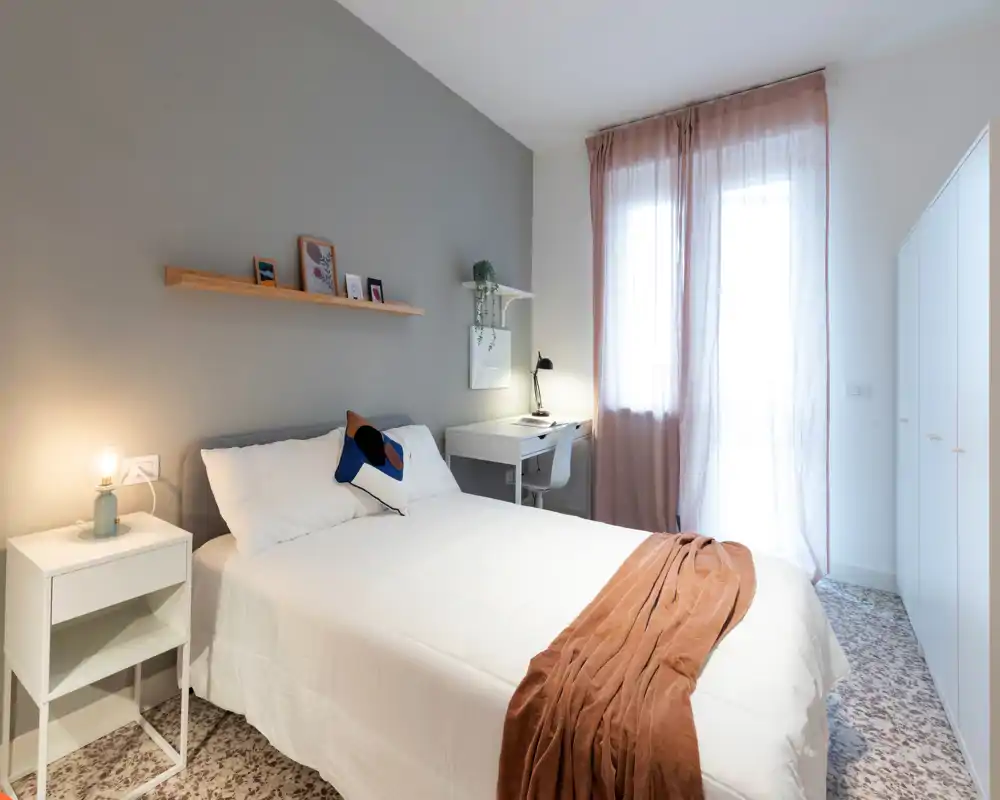 Bright, modern bedroom with a double bed, bedside table and a small work desk by the window. Neutral tones, soft textiles and natural light create a calm, welcoming atmosphere ideal for rental photos.