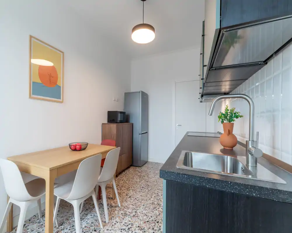 Modern compact kitchen with a dark countertop, stainless sink and a small dining table for four; bright, well-styled space ideal for short-term rentals.