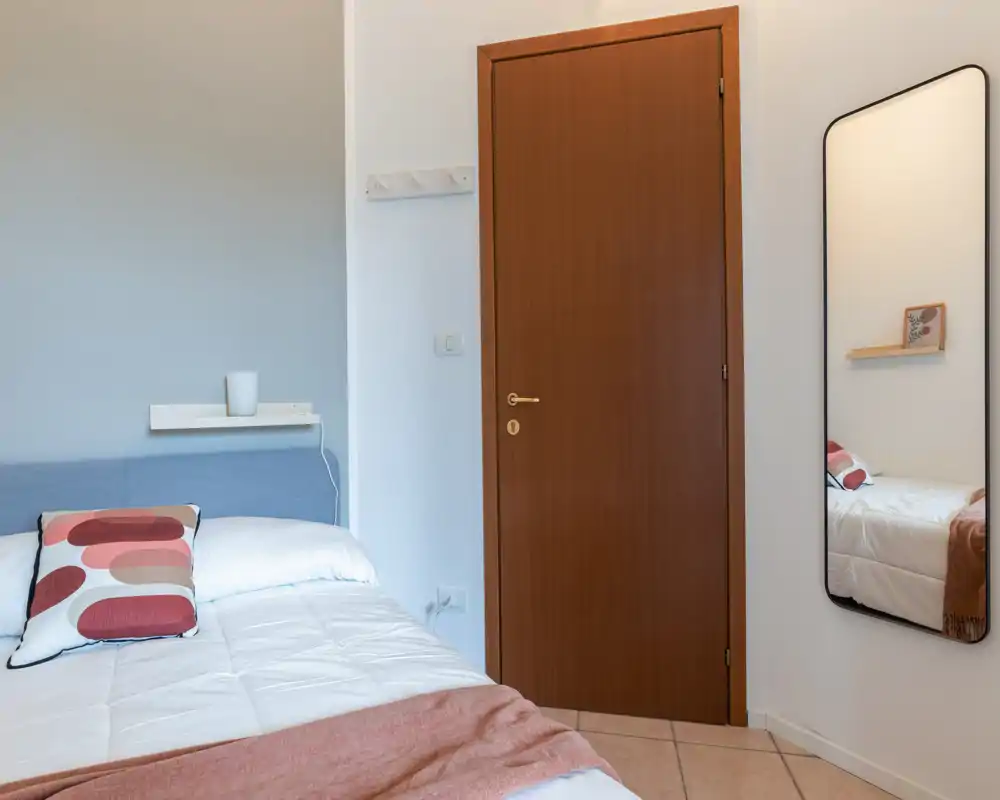 Bright, tidy bedroom with a comfortable double bed, patterned cushion and soft throw; neutral walls and a full-length mirror create a sense of space.