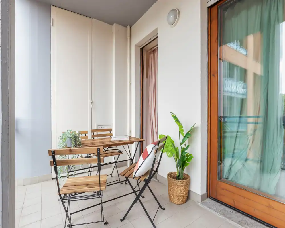 Sunny furnished balcony with a wooden table and folding chairs, decorative plant and cushions — a cozy outdoor spot for breakfast or relaxation.