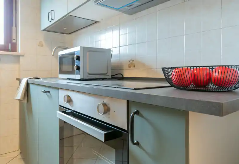 Coin cuisine lumineux avec four électrique, plaque à induction, micro-ondes sur le plan de travail et corbeille de fruits — pratique et soigné pour location courte durée.