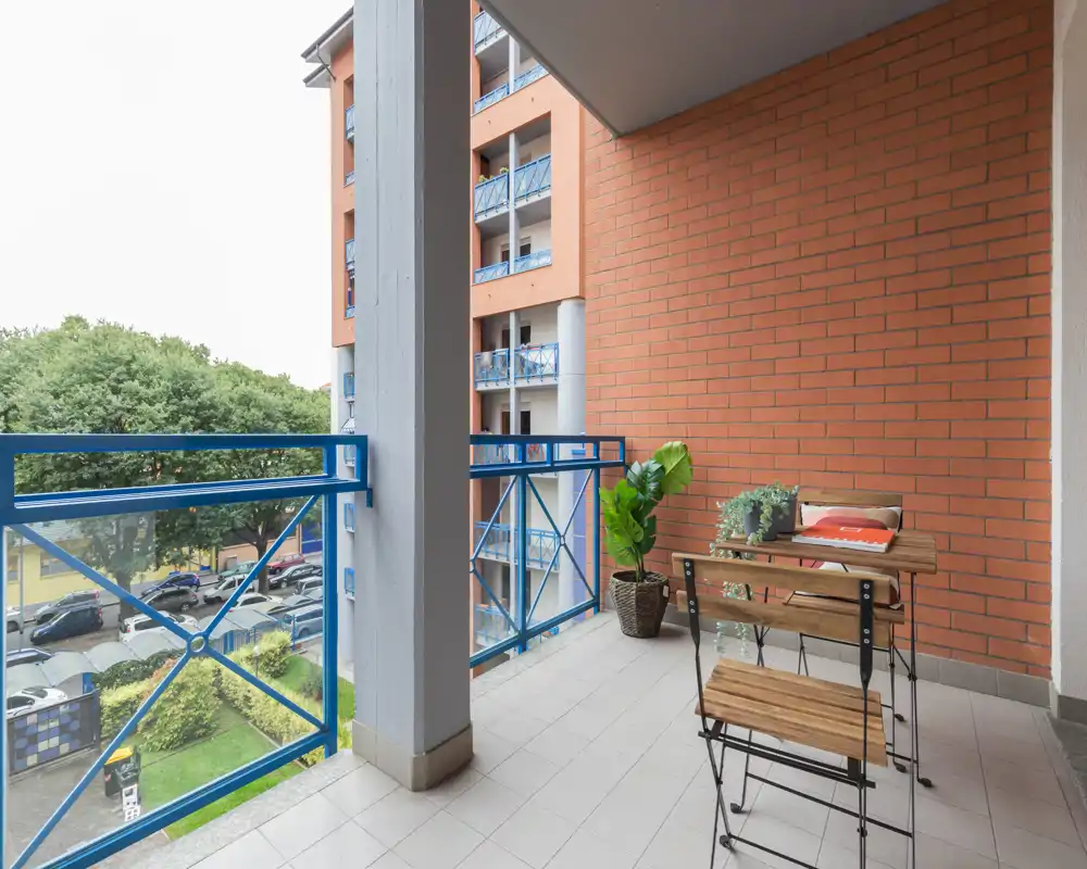 Balcone privato soleggiato con piccolo tavolo e sedie, piante in vaso e vista sulla strada e gli alberi — perfetto per un caffè al mattino.
