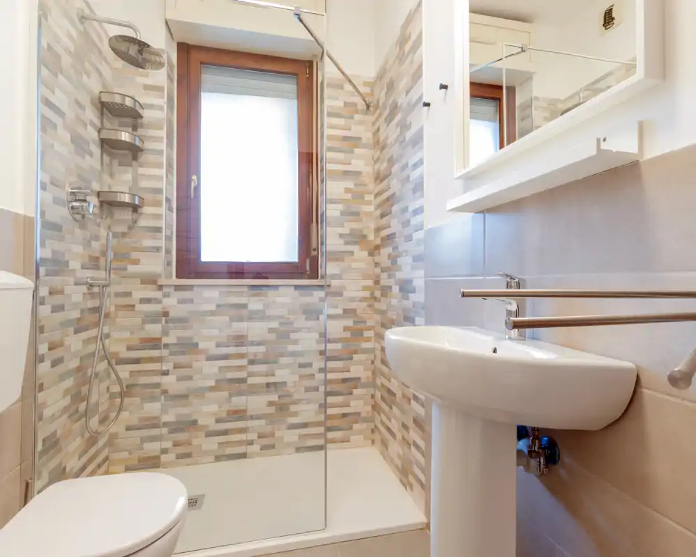 Bagno moderno e luminoso con doccia walk-in, lavabo a colonna e parete piastrellata decorativa per un aspetto pulito e contemporaneo.