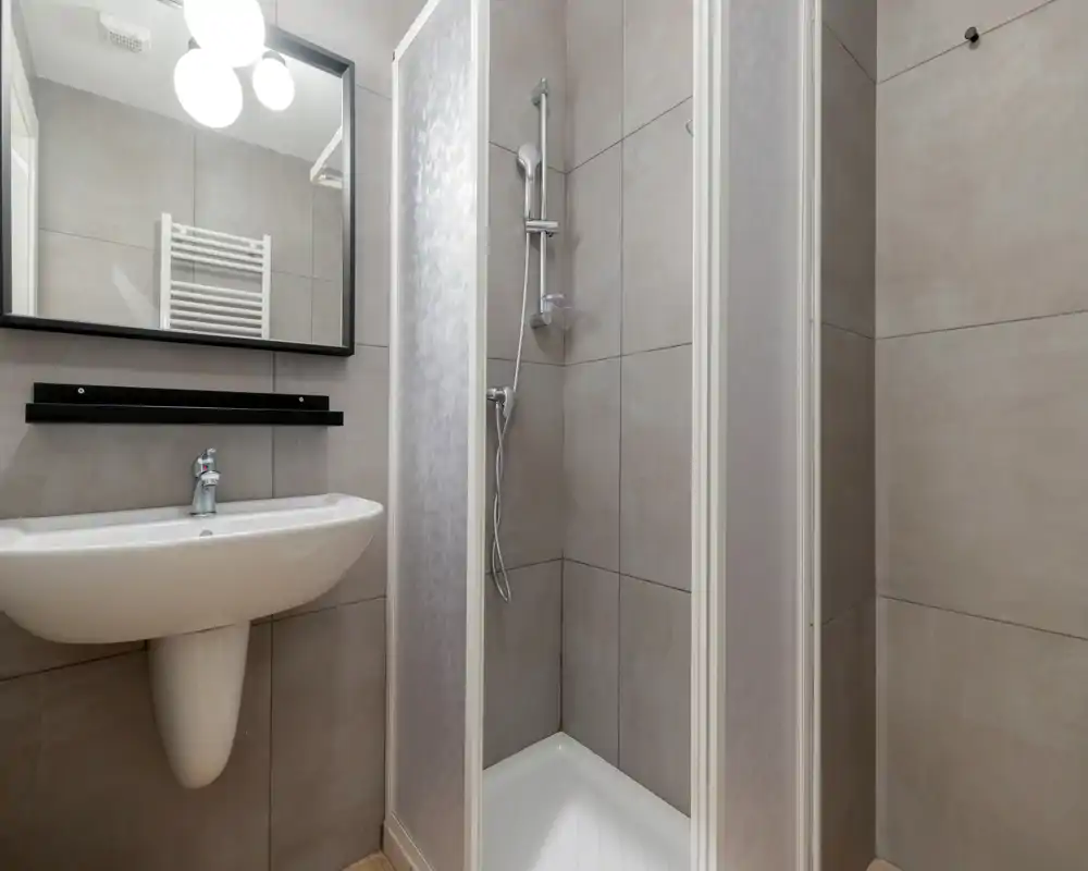 Bagno moderno e compatto con box doccia piastrellato, lavabo a parete e specchio — luminoso, pulito e organizzato in modo efficiente per spazi ridotti.