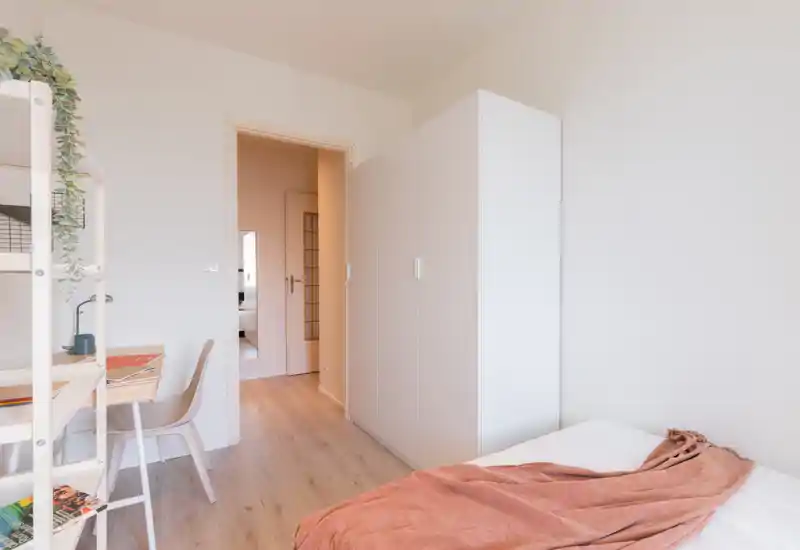 Dormitorio luminoso y minimalista con cama individual cómoda, armario blanco y un pequeño escritorio—ideal para un inquilino. Paleta neutra y luz natural que crean un ambiente tranquilo y aireado.